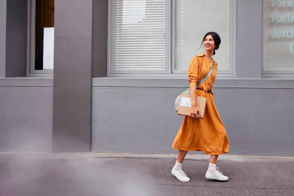 Jeune femme en robe orange qui cherche un carton et qui marche dans la rue